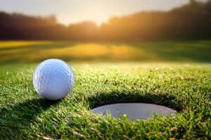 Golf ball near the cup on the green with the sun rising